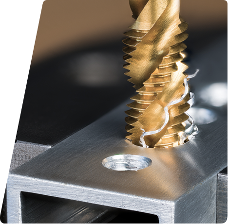 A gold-colored industrial tap cutting threads into a metal workpiece with metal shavings nearby.