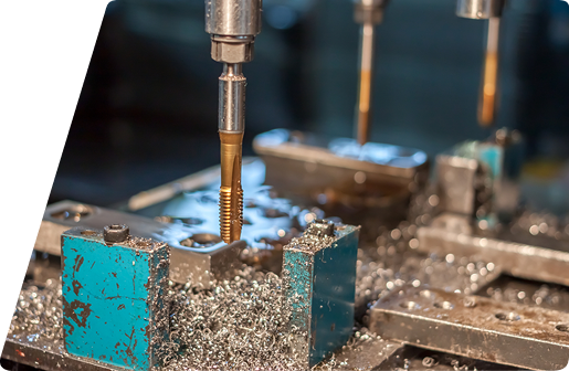 Close-up of a metal tap tool machining a part on a drill press, surrounded by metal shavings.