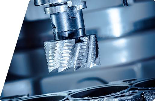 Close-up of a metal milling cutter head positioned over an engine cylinder block in an industrial machining environment.