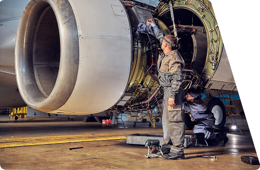 Two mechanics in overalls performing maintenance on a large jet engine inside a hangar.