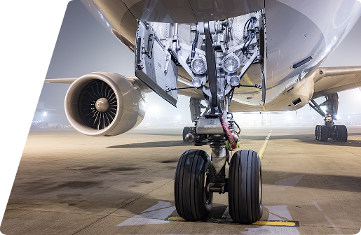 Close-up of an airplane's nose landing gear and jet engine on an airport tarmac at night.