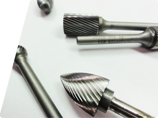 Several metal rotary burr bits with varied tip shapes arranged on a white surface.