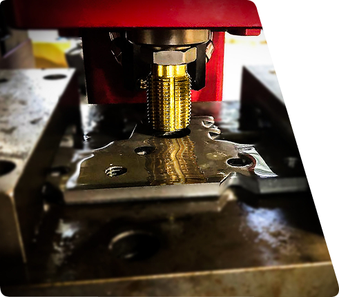 Metal tap tool cutting threads into a lubricated metal part on an industrial machine.